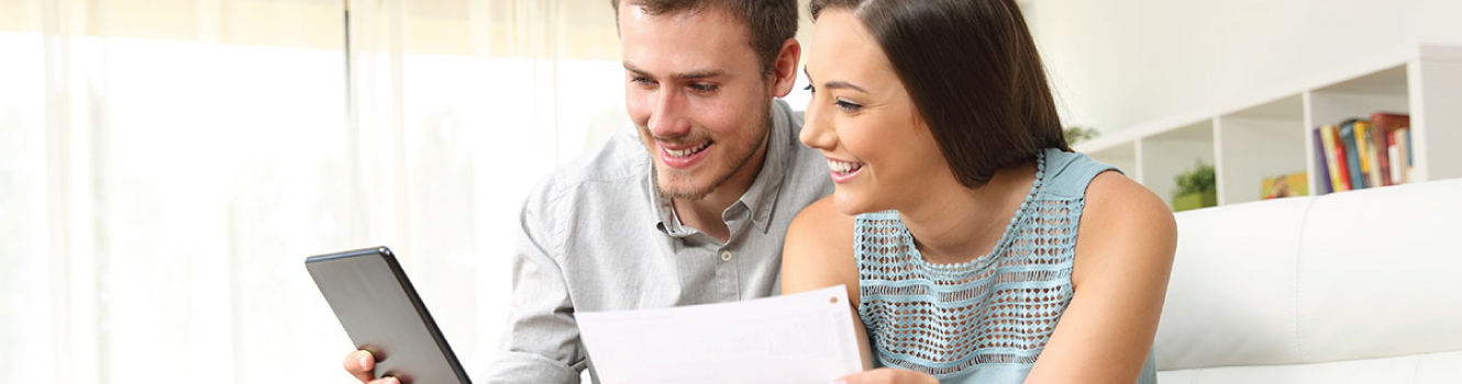 a couple looking at a mobile device with a document in hand.