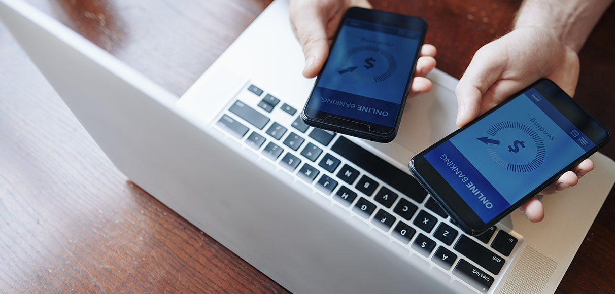 Two hands with two mobile devices on a laptop